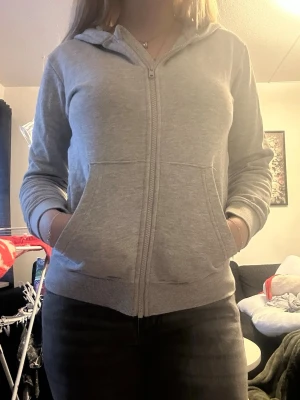 Ljusgrå zip-hoodie med fickor - En stilren ljusgrå hoodie med dragkedja framtill och två stora fickor. Hoodien har en klassisk huva och ribbade muddar vid ärmslut och nederkant. Perfekt för en avslappnad look och enkel att matcha med andra plagg.