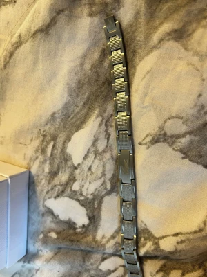 Silverfärgad klocklänk från Lacoste - Stilren klocklänk i silverfärgat metall från Lacoste med klassisk krokodil-logga på spännet. Länken har en snygg kombination av släta och texturerade länkar som ger ett modernt och sportigt intryck. Perfekt för dig som vill uppgradera din klocka med en ikonisk detalj.