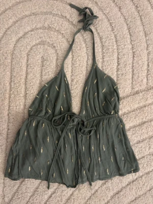 Grön mörkgrön guld glitter linne halterneck öppen rygg sommar topp blus rare knyt rosett bow - Gulligt och unikt linne som är köpt utomlands i Spanien. Grönt med guldigt/glittrigt mönster. Riktigt snygg att ha över bikini till stranden ☀️Står ingen storlek, gissar att det är ONE SIZE, men passar bäst som XS-S. Stretchig!