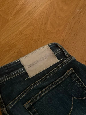 Jacob Cohen, BARD - Snygga mörkblå jeans från Jacob Cohen med klassisk femficksdesign och kontrastsömmar. Jeansen har en vit patch med logga bak i midjan och är tillverkade i ett mjukt denimtyg. Perfekta för en trendig och avslappnad look.