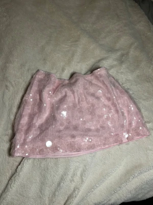 Rosa kort paljettkjol - Supersöt rosa kjol med glittriga paljetter och mesh-tyg över ett mjukt foder. Kjolen är kort och ger en trendig look. Perfekt för dig som gillar att sticka ut med lite extra glitter eller för fest i sommar. Liten slitt på sidan