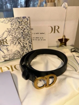 Svart bälte från Dior med gulddetalj - Snyggt svart bälte från Dior med klassiskt CD-spänne i guld. Bältet är smalt och stilrent, perfekt för att lyfta vilken outfit som helst. Kommer med originalpåse och förpackning.