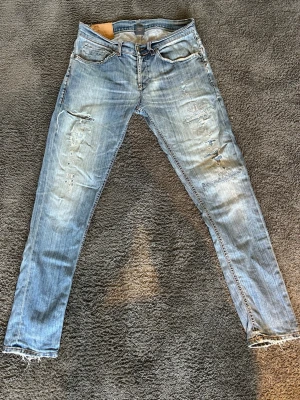Dondup george jeans - Säljer ett par ljusblå skinny jeans med slitningar och trasiga detaljer på benen. Jeansen har klassisk femficksmodell, låg midja och råa kanter vid bensluten. Perfekta för en avslappnad och trendig look.