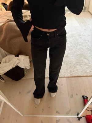 Svarta raka jeans med hög midja - Säljer ett par svarta jeans med rak passform och hög midja. Klassisk femficksmodell med knapp och dragkedja framtill. Jeansen har en tidlös look och passar perfekt till en avslappnad stil. Materialet är kraftigt denim i bomull.