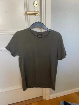 Mörkgrön basic t-shirt från OJ - En enkel och stilren mörkgrön t-shirt från Oscar Jacobsson. Modellen har rund halsringning och korta ärmar. Perfekt att matcha med jeans för en clean look. Tillverkad i mjuk bomull för skön känsla hela dagen.