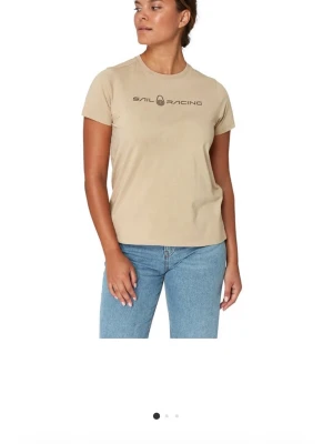 Beige t-shirt från Sail Racing - Säljer en beige t-shirt från Sail Racing med logotyp på bröstet. T-shirten har korta ärmar och rund halsringning. Materialet är mjuk bomull som känns skönt mot huden. Perfekt för dig som gillar stilrena plagg med sportig touch.