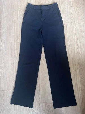 Svarta raka kostymbyxor - Snygga svarta kostymbyxor med raka ben och pressveck. Byxorna har hällor för skärp och sidofickor. Klassisk och stilren modell som passar till många olika looks. Materialet ser ut att vara en mjuk och lite stretchig blandning.