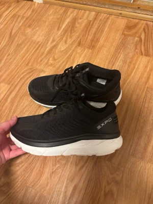 Svarta EXPO sneakers med vit sula - Svarta sneakers från EXPO med vit, chunky sula och ventilerande mesh-ovandel. Skorna har klassisk snörning och låg profil. Perfekta för dig som gillar sportig och stilren look. Snygga detaljer och bekväm passform.