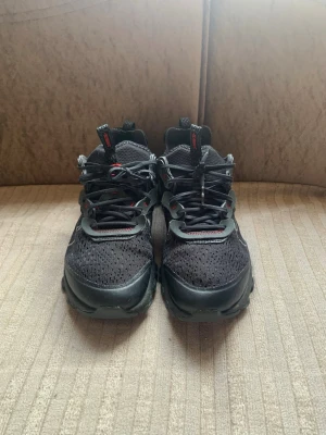 Svarta Nike React Element sneakers med box  - Säljer ett par svarta Nike React Element sneakers med mesh-ovandel och detaljer i syntet. Skorna har svarta och röda accenter, samt den klassiska vita Swoosh-loggan på sidan. Sulan är chunky och ger grym komfort. Perfekta för dig som gillar streetwear och sportig stil.