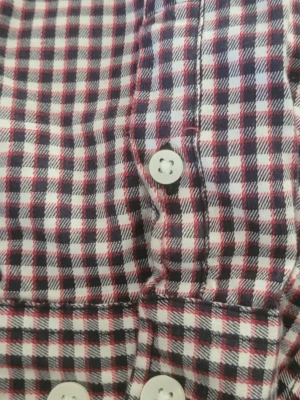  2 Rutiga skjortor i bomull med knappar - Klassiska långärmade skjortor med små rutor i vitt, rött och mörkblått. Skjortorna har vita knappar framtill och är tillverkad i mjuk bomull. Perfekt för en avslappnad men ändå stilsäker look.