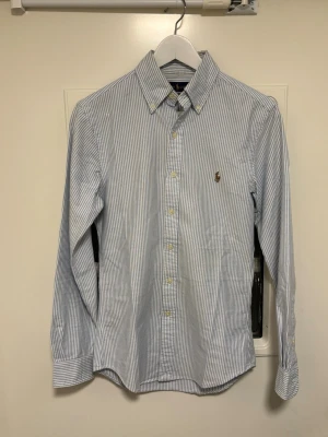 Ralph Lauren Skjorta - Vit/blå randig polo ralph Lauren skjorta XS-Slim fit Skick 9/10, inga defekter Mått: Längd 65cm, bredd 45cm Pris kan diskuteras! Skriv vid funderingar!