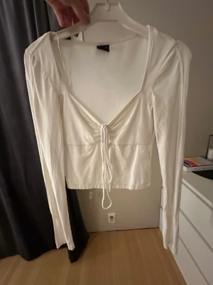 Vit topp med snörning - Trendig vit topp med lång ärm och snygg snörning framtill som ger en cool v-ringad look. Perfekt att styla med jeans eller kjol för en fräsch outfit. Mjuk och skön känsla, passar dig som gillar stilrena plagg med en twist.