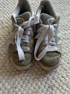 Adidas campus grå  - Snygga grå sneakers från Adidas med klassiska vita ränder på sidorna och vit logga på plösen. Skorna har vita skosnören och en låg profil. Ovandelen är i mocka och textil, sulan är i gummi. Perfekta för en avslappnad streetstil. SKRIV FÖR FLER BILDER! Har dock inte tvättat de en men gör så gott jag kan innan jag skickar dem🤍🤍 