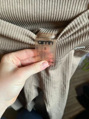 Beige ribbade tights från Aim'n - Säljer ett par beige ribbade tights från Aim'n i storlek S. De har hög midja och är tillverkade i ett stretchigt material med 92% polyamid och 8% elastan. Perfekta för träning eller chill dagar. Snygg passform och sköna att bära.