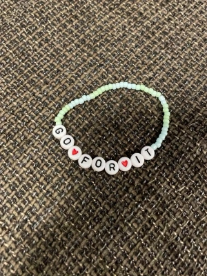 Pärlarmband med text GO FOR IT - Sött pärlarmband med små pastellgröna och ljusblå pärlor samt vita bokstavspärlor som bildar texten 'GO FOR IT' med röda hjärtan. Perfekt accessoar för att peppa dig själv eller någon annan. Elastiskt band för enkel användning.