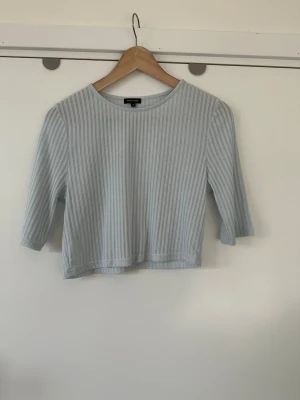 Ljusblå River Island ribbad croppad topp - storlek 40/L - Fin ribbad topp från River Island i storlek 40 /L med trekvartsärmar och rund halsringning. Toppen har en figurnära passform och är designad med vertikala ränder som ger en smickrande silhuett. Perfekt för en avslappnad men stilfull look. Mycket fint skick, som ny!  Skickas mot porto, kan även hämtas i Stockholm.