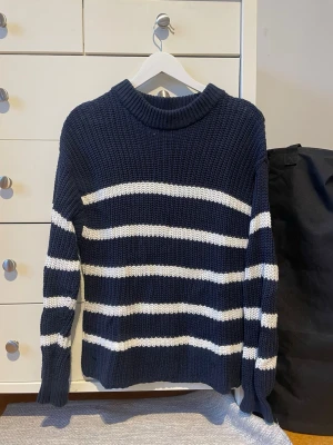 Marinblå stickad tröja med vita ränder - Snygg marinblå stickad tröja med breda vita horisontella ränder. Grovstickad i ett mjukt material som passar perfekt för kyligare dagar.