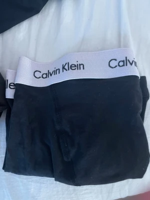 Svarta kalsonger från Calvin Klein - Säljer ett par svarta kalsonger från Calvin Klein med bred vit resår och logga i svart. Klassisk boxermodell med mjukt och stretchigt material för skön passform. Perfekta för dig som gillar stilrena underkläder med ikonisk design.