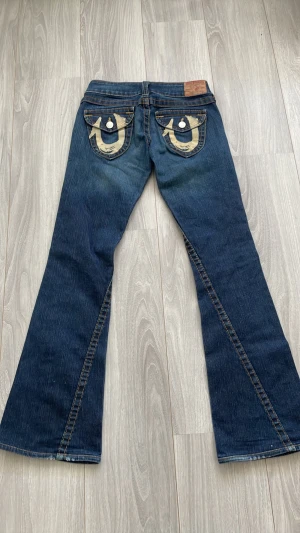 Mörkblå True religion bootcut jeans  - Säljer ett par mörkblå True religion jeans som är bootcut med snygga broderade bakfickor i beige. Jeansen har låg midja och utsvängda ben. 💗