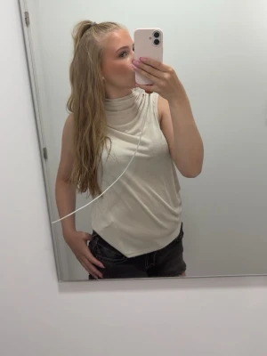 Beige ärmlös polotopp - Snygg beige ärmlös polotopp med hög hals. Den är beige glittrig och väldigt skön men kommer inte till användning. 