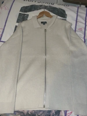 Beige ziptröja från Zara - Säljer en stilren beige ziptröja från Zara med diskret ribbad struktur. Tröjan har hel dragkedja framtill, hög krage och långa ärmar. Perfekt för lager på lager och enkel att matcha med olika outfits.