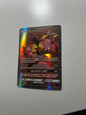 Buzzwole GX Pokémonkort Ultra Beast - Säljer ett Buzzwole GX Ultra Beast Pokémonkort med holografisk yta. Kortet har färger i rött, gult och svart med metallic-effekt och tydliga attacker som Jet Punch och Knuckle Impact. Perfekt för samlare eller Pokémonfans som vill utöka sin kortlek.