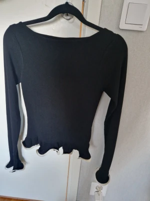Svart långärmad tröja Gina Tricot - Svart långärmad tröja från Gina Tricot med vågiga kanter vid ärmslut och nederkant. Tröjan har en tight passform och är tillverkad i ett mjukt stickat material. Perfekt att styla med jeans eller kjol för en trendig look