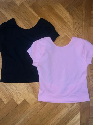 Svart och rosa toppar med öppen rygg - Två enkla och stilrena toppar i svart och ljusrosa. Båda har rund halsringning, korta ärmar och öppen rygg, perfekta att matcha med jeans eller kjol. Materialet känns mjukt i bomull. Snygga basplagg för en clean look. Köpta på Edikted i USA. 1 för 200kr, 2 för 350kr
