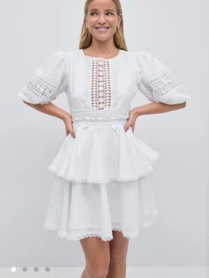 Vit spetsklänning med volanger - Superfin vit klänning från Gina med kort kjol, volanger och spetsdetaljer. Klänningen har puffiga ärmar och vackert broderad spets framtill och i midjan. Perfekt för sommarens alla tillfällen, riktigt söt och trendig design.