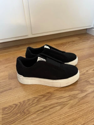 Svarta slip-on sneakers från 157 - Svarta sneakers i slip-on-modell från lager 157 med bred resår över vristen och vit sula. Skorna är i textilmaterial och har en minimalistisk design utan snörning. Perfekta för en clean och avslappnad stil. Använda en gång och är i storlek 38 men passar även 39, pris och frågor går att diskutera💕