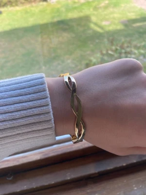 Guldigt tvinnat armband - Snyggt armband i guldfärgad metall med tvinnad design. Armbandet har en stilren och modern look som passar perfekt till olika outfits. Enkel att ta på och av tack vare öppningen baktill. Perfekt accessoar för dig som gillar minimalistisk stil. Den är lite sönder där med öppningen med funkar ändå bra☺️