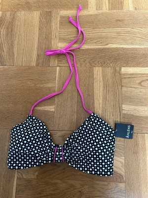 Prickig bikiniöverdel med rosa band - Snygg prickig bikiniöverdel från Åhléns med rosa knytband i nacken. Inläggen går att ta ut om man vill. Bikinitoppen är helt ny.