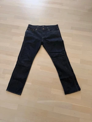 Mörkblå Hugo Jeans - Hugo Boss stretchjeans i mörkblå denim med klassisk och stilren design. Slim/straight fit med bekväm stretch för bra passform och rörelsefrihet. Jeansen har mörk tvätt med diskreta slitningar/fade-effekter, orange kontrastsömmar och läderpatch med BOSS-logga baktill.  Detaljer:  * Märke: BOSS Hugo Boss * Modell: Stretch * Färg: Mörkblå denim * Passform: Slim/Straight fit * Material: Stretchdenim * Skick: Fint begagnat skick, se bilder för detaljer  Perfekta både till vardag och mer uppklädda out