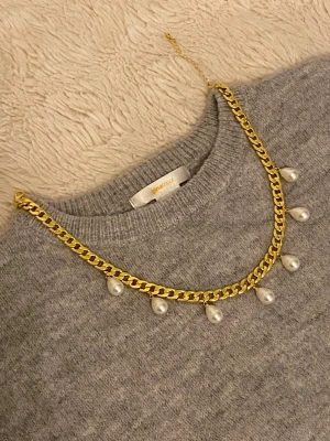 Guldfärgat halsband med pärlhängen - Snyggt guldfärgat rostfritt halsband med chunky kedja och sju droppformade vita pärlhängen. Halsbandet har justerbar längd och ger en trendig touch till din outfit. Perfekt för dig som gillar statement-smycken och vill sticka ut.