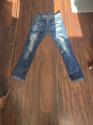 Dsquared2 jeans  - Säljer ett par mörkblå jeans med coola färgstänk och slitningar på benen. Jeansen har klassisk femficksmodell och smal passform. Perfekta för dig som vill ha en unik och kreativ look.
