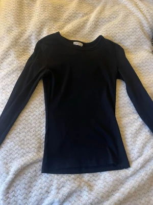 Svart långärmad topp från Gina Tricot - En enkel och stilren svart långärmad topp från Gina Tricot, kollektionen 'basically basics'. Modellen är tight och har rund halsringning. Perfekt att matcha med jeans eller kjol för en clean look.