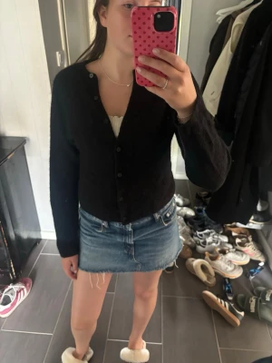 Svart kofta med knappar - En svart, långärmad kofta med knäppning framtill. Koftan har en enkel och klassisk design med rund halsringning och mjukt material. Perfekt att slänga över en topp eller klänning för en stilren look.
