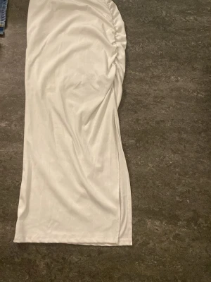 Vit långkjol med rynkade detaljer och slits - Snygg vit långkjol med rynkade detaljer på ena sidan. Kjolen har en rak passform med en slits på sidan och är tillverkad i ett mjukt material som ger en stilren look. Perfekt för dig som vill ha en enkel men trendig kjol till din garderob. Kjolen är i storlek ca men är så strentchig så det passar till nästan alla den är väldigt töjbar