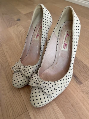 Prickiga pumps med rosett  - Snygga pumps köpte i Italien i cremevitt med svarta prickar och en söt rosett framtill. Skorna har klassisk rund tå och hög smal klack. Perfekta för dig som gillar retrostil och vill sticka ut med ett unikt mönster.
