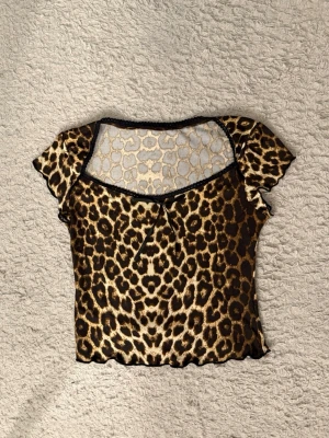 Leopardmönstrad topp  - Säljer en leopardmönstrad topp med korta ärmar och transparent mesh upptill. Toppen har en liten rosett framtill och svarta kantdetaljer. Perfekt för dig som vill sticka ut med en djärv look.