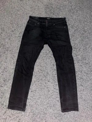  Jack & Jones - Svarta slim fit jeans från Jack & Jones med klassisk femficksdesign och normal midja. Jeansen har smal passform och är tillverkade i stretchigt denimtyg för extra komfort. Perfekta för en stilren och modern look.