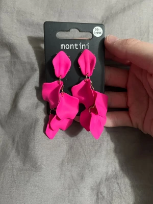 Rosa örhängen från Montini/köpt på ur och pen - Snygga örhängen från Montini i en stark rosa färg. De har flera lager av bladliknande former som hänger i olika nivåer. Örhängena har guldfärgade detaljer och är perfekta för att sticka ut med en färgklick. Ej använda då jag köpte dom i en mysterybox 
