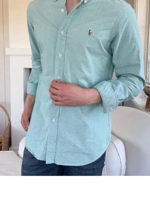 Ralph Lauren skjorta - Snygg ljusblå skjorta från Ralph Lauren med klassisk krage och knäppning framtill. Skjortan har lång ärm och den ikoniska broderade loggan på bröstet. Perfekt till jeans eller chinos för en clean look.