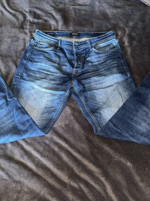 Jeans - Snygga blå jeans från Jack & Jones med klassisk femficksdesign och slitna detaljer framtill. Jeansen har en rak passform och är tillverkade i denim med en cool tvättad look. Perfekta för en avslappnad stil.