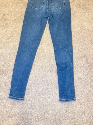 Blå skinny jeans med stretch - Snygga blå skinny jeans med lätt slitning och smal passform. Jeansen har klassisk femficksdesign och är tillverkade i stretchigt denimtyg för extra komfort. Perfekta att matcha med sneakers eller boots.