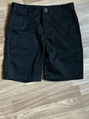 Svarta shorts från Volcom - Svarta klassiska shorts från Volcom med normal passform. Shortsen har fickor fram och bak, bälteshällor och knappstängning. Perfekta för sommaren och enkla att matcha med olika outfits. Nypris 699 kr, köpt på Zalando.
