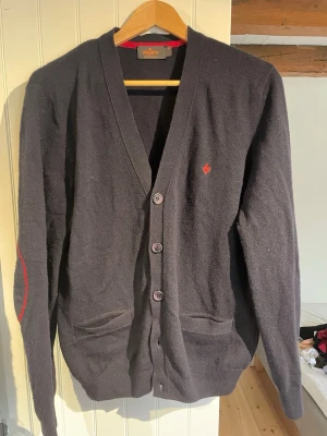 Fin Morris kofta i 100% merinoull - En av Morris fina tröjor från 100% merinowool kollektionen som enligt mig har den bästa kvaliteten av merinoull och ull överlag. Len mot huden och kliar inte samt värmer väl samtidigt som materialet andas. Mörkblå med röda detaljer i storlek M. Använd men inga skador eller tecken på användning.