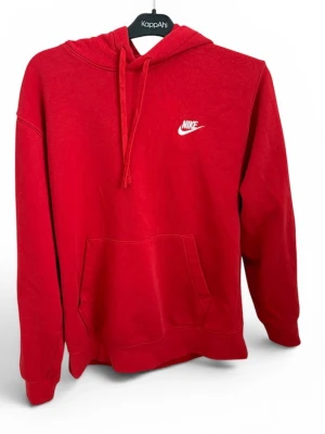 Röd hoodie från Nike med logga - Riktigt snygg röd hoodie från Nike med klassisk vit logga på bröstet. Hoodien har huva med dragsko och en stor känguruficka framtill. Tillverkad i mjukt material som känns skönt mot huden. Perfekt för en avslappnad och sportig stil.