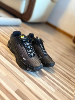 Nike Air Max Plus TN Svarta sneakers - Säljer ett par Nike Air Max Plus TN sneakers i svart med detaljer i silver och gult. Skorna har en sportig design med mesh och syntetmaterial, klassiska TN-loggan på plösen och robust sula. Perfekta för dig som gillar streetstyle och ikoniska modeller.