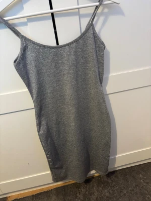 kort grå klänning - En enkel och stilren grå klänning med smala axelband och rak passform. Klänningen är ärmlös och har en mjuk, bekväm känsla som passar perfekt till varmare dagar.